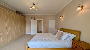 A bedroom with a wooden bed, a wooden nightstand, a wardrobe, and a ceiling light fixture. - Charming Two-Bedroom House in London (Greater London)