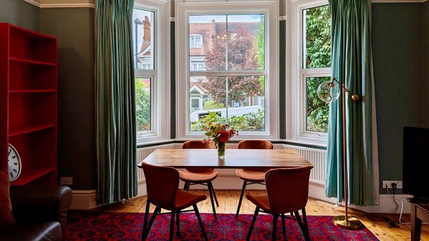 A dining area with a round table, four chairs, a clock, and a red bookshelf. - Charming Two-Bedroom House in London (Greater London)