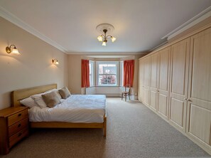 A bedroom with a bed, a wooden dresser, a chair, a wardrobe, and a window with curtains. - Charming Two-Bedroom House in London (Greater London)