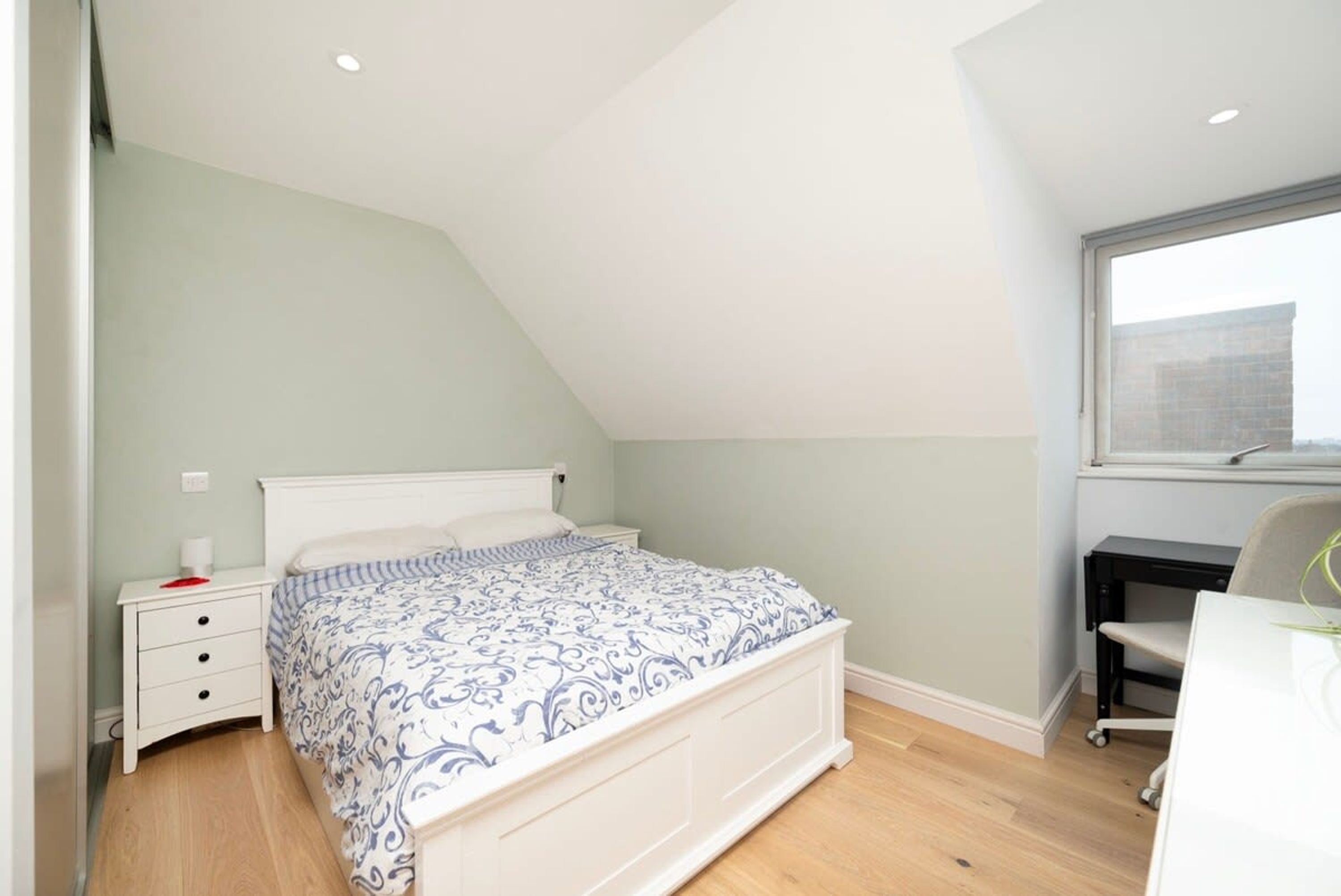 A bedroom with a sloped ceiling, a bed with a patterned bedspread, a nightstand, a desk, and a chair.