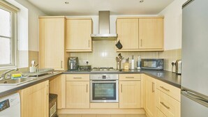 A modern kitchen with wooden cabinets, a built-in oven, a microwave, and a stainless steel refrigerator. - Charming 2-Bedroom Flat in South Croydon (South Croydon)