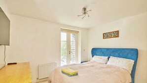 A bedroom with a bed, a wooden desk, a radiator, and a window. - Charming 2-Bedroom Flat in South Croydon (South Croydon)