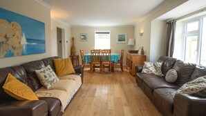 A living room with two leather sofas, a wooden dining table, and a blue tablecloth. - Spacious Home Near Porthtowan Beach (Porthtowan)