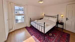 A bedroom with a bed, a nightstand, a window, and a radiator.