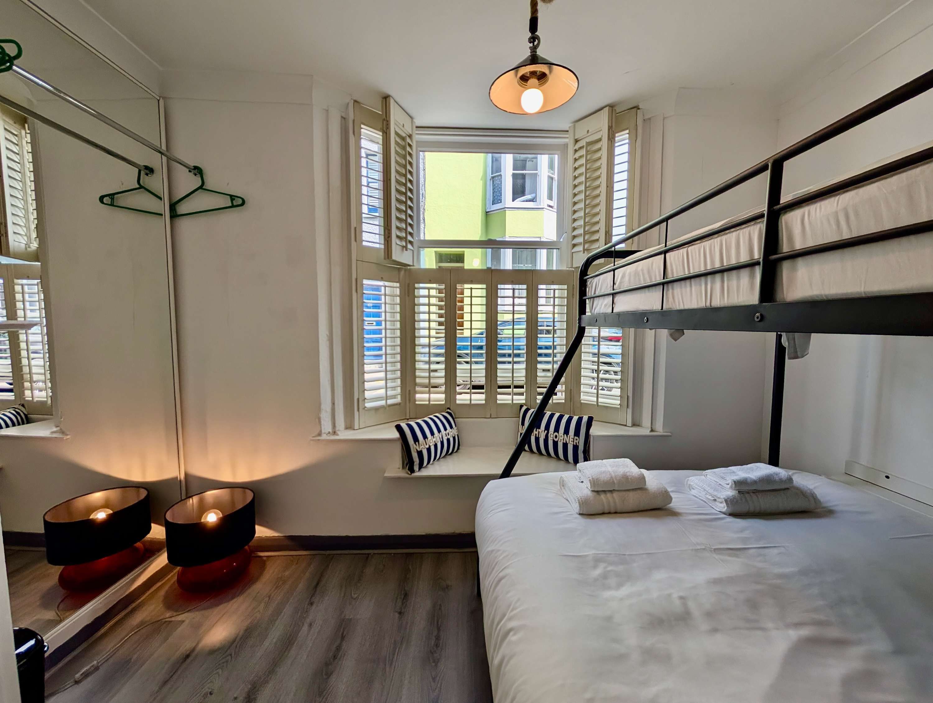 A room with a bunk bed, a window with shutters, a mirror, and a hanging light fixture.