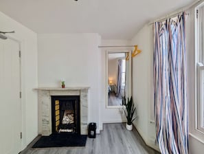 A hallway with a fireplace, a mirror reflecting the room, a striped curtain, and a potted plant. - Charming House With Balcony Near Brighton Beach (Brighton and Hove)