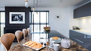 A modern kitchen with a marble countertop, wooden chairs, and a dining table. There are plates of food, cups, and a teapot on the table. - Stylish Penthouse with London Views (London)