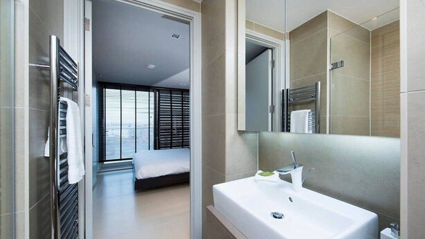 A modern bathroom with a large sink, a mirror, and a shower area. - Stylish Penthouse with London Views (London)
