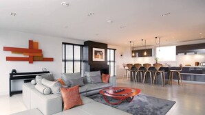 A modern living room with a grey sofa, a red coffee table, and a kitchen area with a dining set. - Stylish Penthouse with London Views (London)