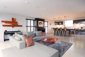 A modern living room with a grey sofa, a red coffee table, and a kitchen area with a dining set. - Stylish Penthouse with London Views (London)