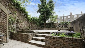 A brick patio with steps leading to a garden area, surrounded by a brick wall and a tree. - Cozy Studio with Private Garden in London (London)