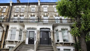 A multi-story townhouse with a central black door, white-framed windows, and a brick facade. - Cozy Studio with Private Garden in London (London)