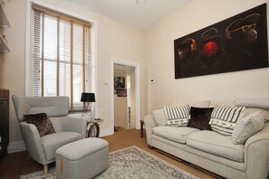 A living room with a grey armchair, a beige sofa, and a large abstract painting on the wall. - Charming Victorian Home in Westminster (Greater London)