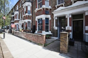 A row of red brick terraced houses with white window frames and a black gate. - Charming Victorian Home in Westminster (Greater London)