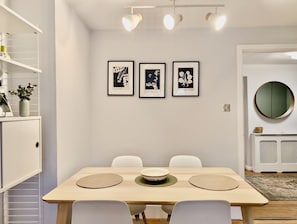 Ein Essbereich mit einem Holztisch, weißen Stühlen und drei gerahmten Pflanzenbildern an der Wand.