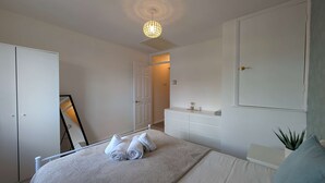 A bedroom with a bed, a wardrobe, a mirror, and a ceiling light. - Comfortable 2-Bedroom house with free parking (Greater London)