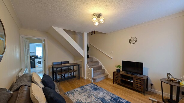 A living room with a sofa, a coffee table, a TV, and a staircase leading to a kitchen. - Comfortable 2-Bedroom house with free parking (Greater London)