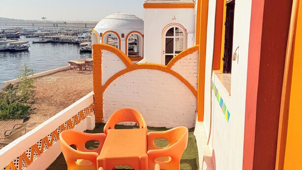 A terrace with orange plastic chairs and a table, overlooking a marina with boats. - Wanas kato  (Aswan)