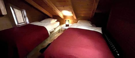 A single room with two beds, a nightstand, and a window.