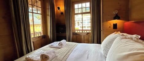 A hotel room with a bed, two windows, a lamp, and a view of the outside.