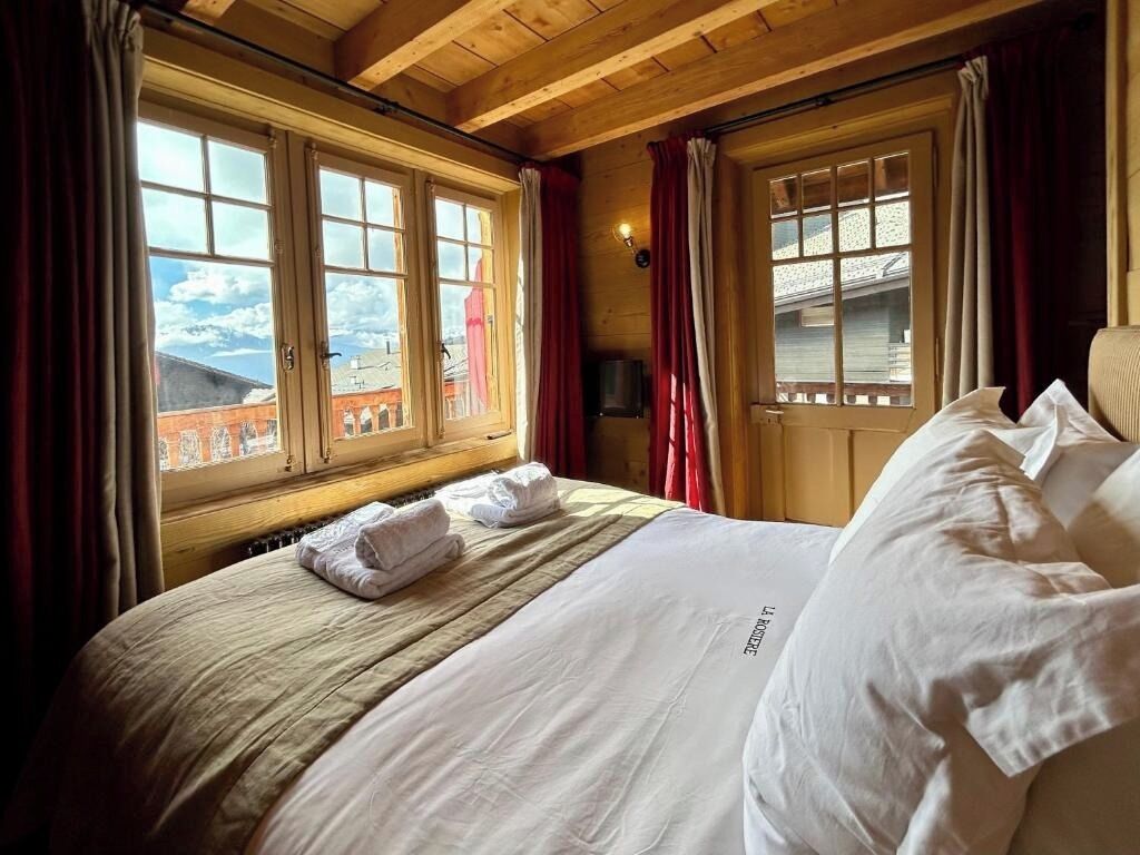Ein Hotelzimmer mit einem großen Bett, Holzbalkendecke und Fenstern mit Vorhängen.