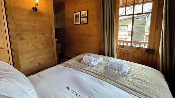 A wooden room with a bed, a wall-mounted light, and a window with curtains. - -La Rosière- Premium Chalet, in the center of Villars-sur-Ollon (Villars-sur-Ollon)