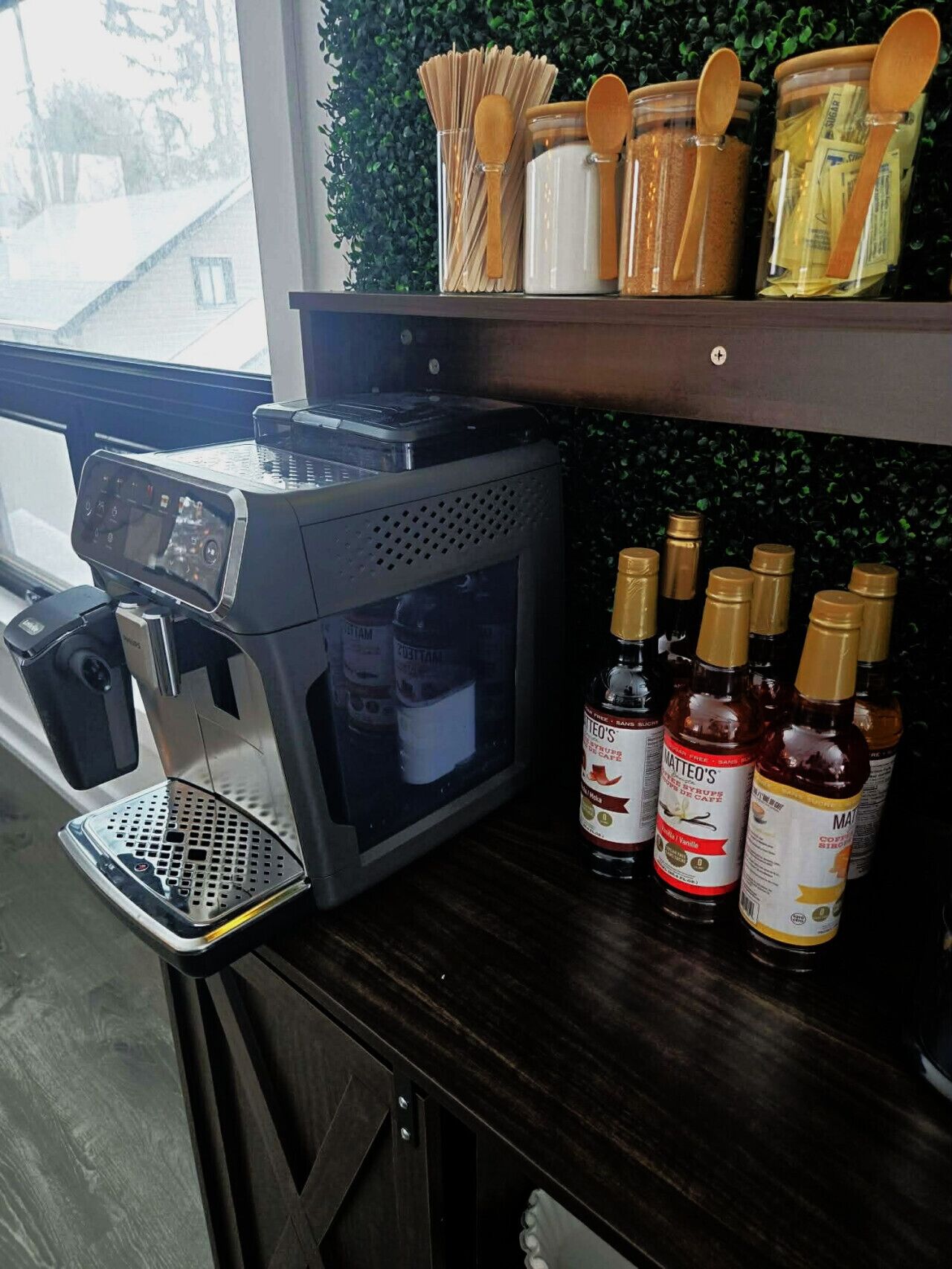 Una máquina de café, dosificadores de azúcar y almíbar, y botellas de almíbar sobre una encimera.