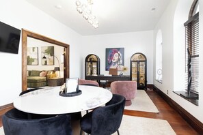 A modern living room with a round white table, black chairs, a green sofa, and a large painting.