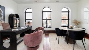 Een moderne eethoek met een ronde tafel, zwarte en roze stoelen, en een kroonluchter.