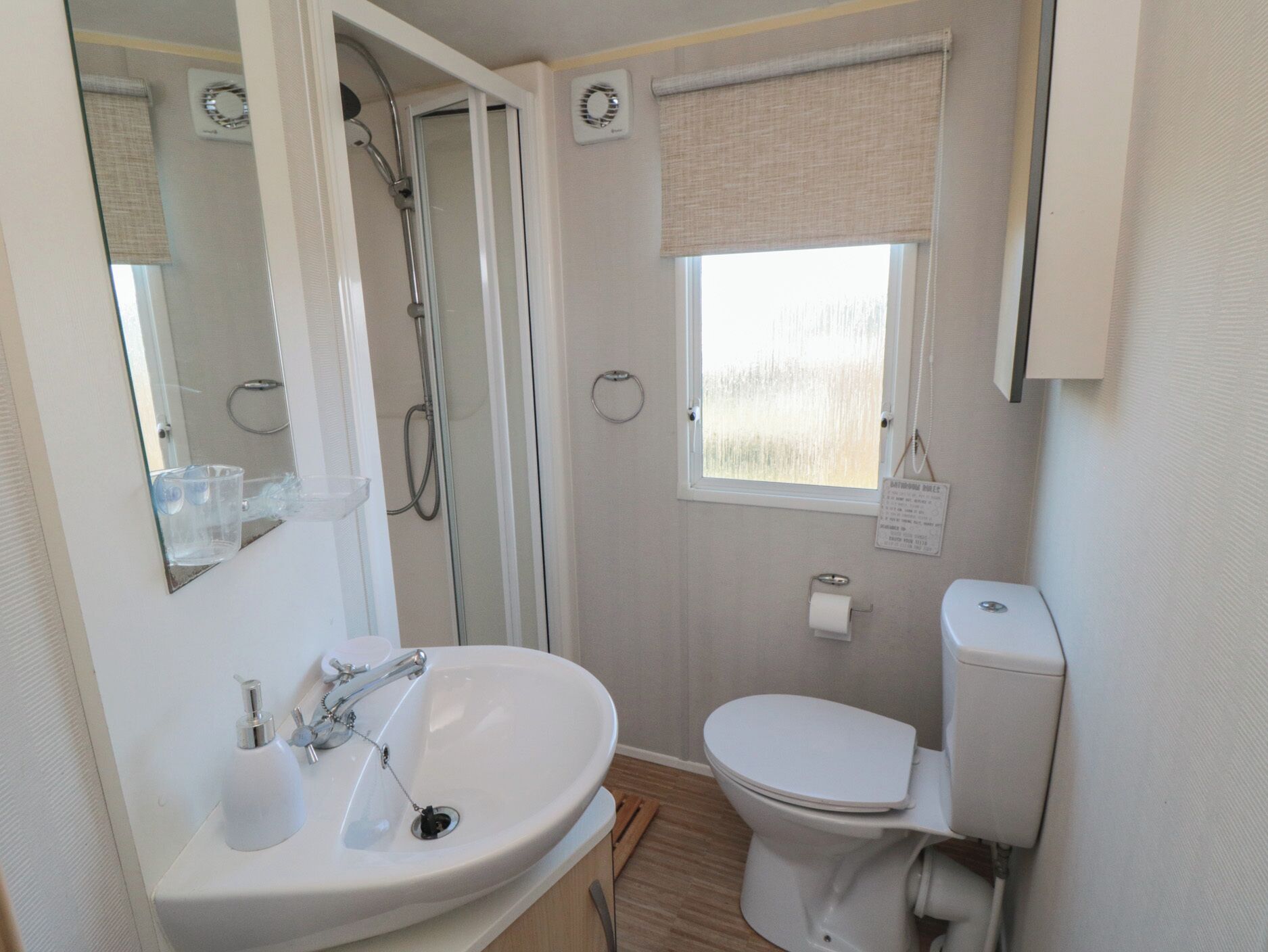Ein kleines Badezimmer mit Waschbecken, Toilette, Dusche und einem kleinen Fenster.