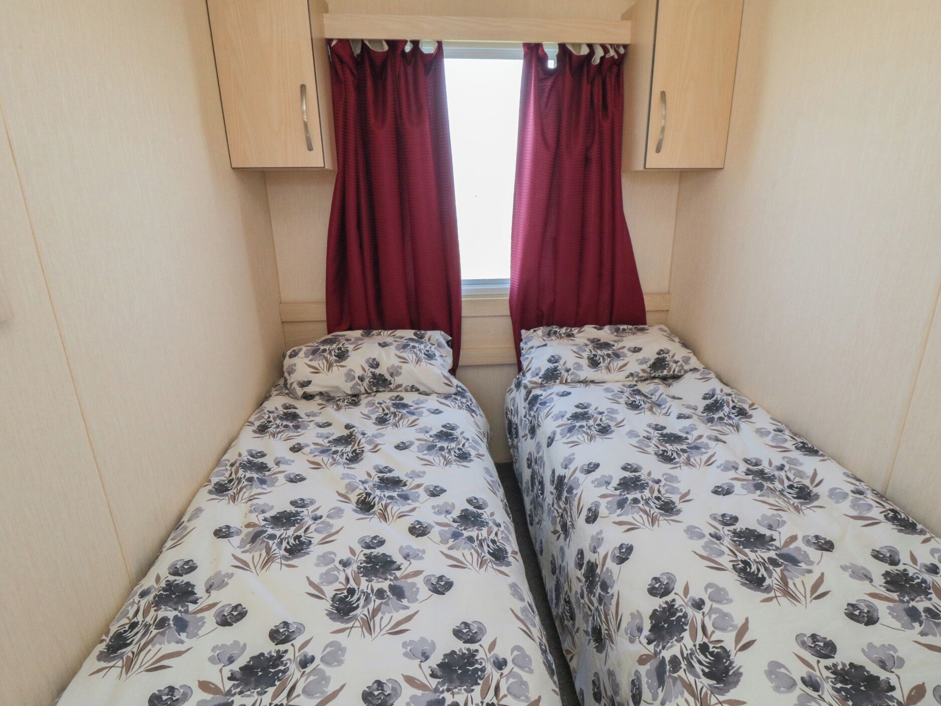 A small, cozy room with two beds, wooden cabinets, and red curtains.