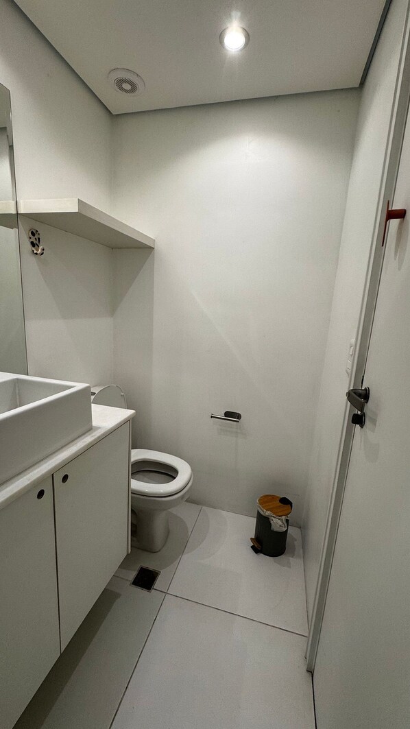 A small, modern bathroom with a toilet, a sink, and a mirror. - HOTEL PERDIZES - Flat Executivo - 1402 (São Paulo)