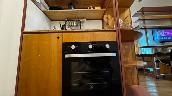 Une cuisine compacte dotée d’un four encastré, de meubles en bois et d’un petit plan de travail.