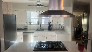 Une cuisine moderne avec des armoires blanches, un réfrigérateur en acier inoxydable, une cuisinière à gaz et un ventilateur de plafond.