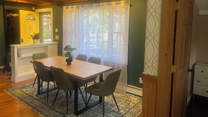Un coin repas avec une table et des chaises en bois, une plante en pot et une fenêtre ornée de rideaux légers.