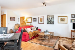 A living room with a red sofa, wooden coffee table, and framed pictures on the wall.