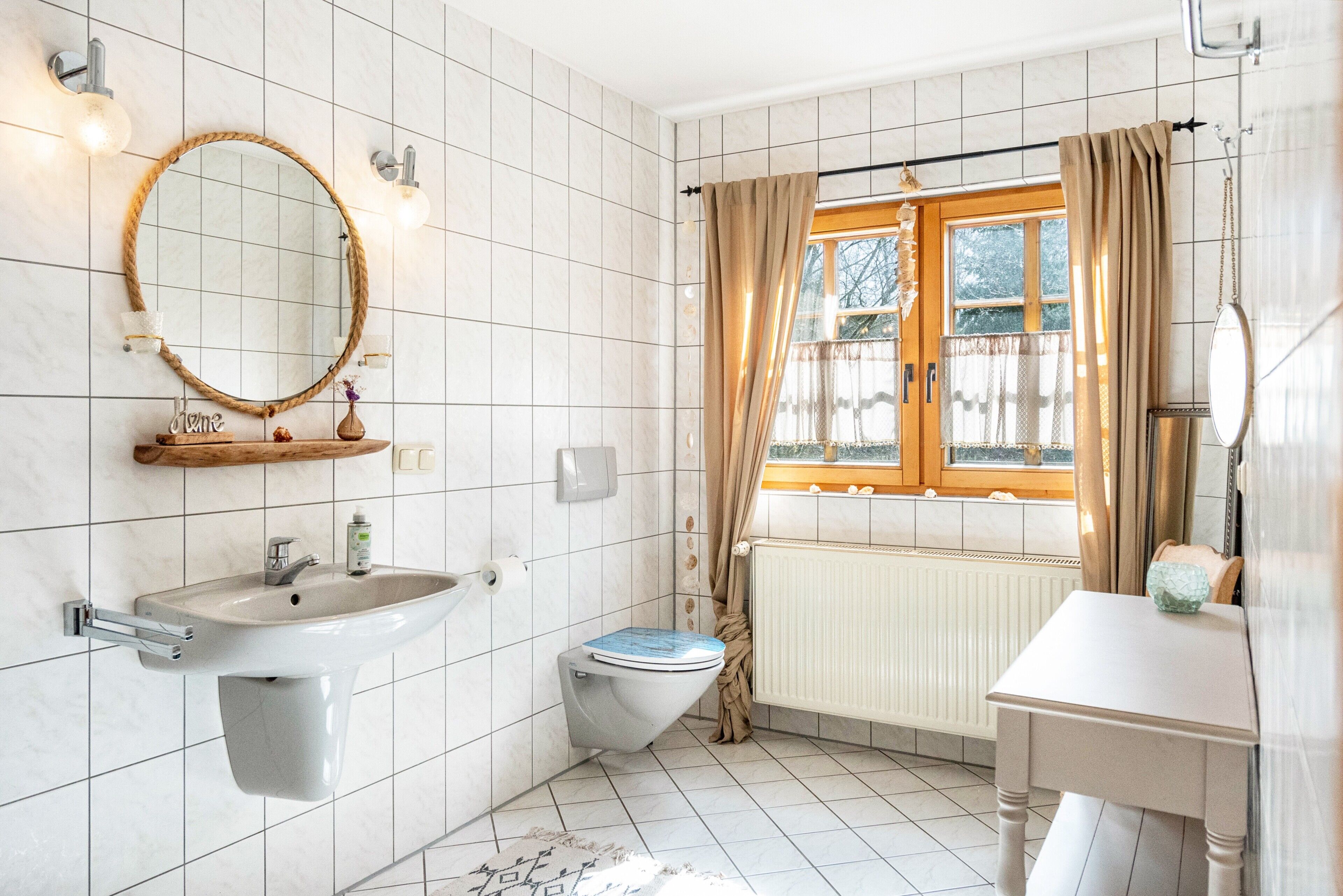 Une salle de bain équipée d’un lavabo, de toilettes, d’un miroir et d’une fenêtre avec des rideaux.