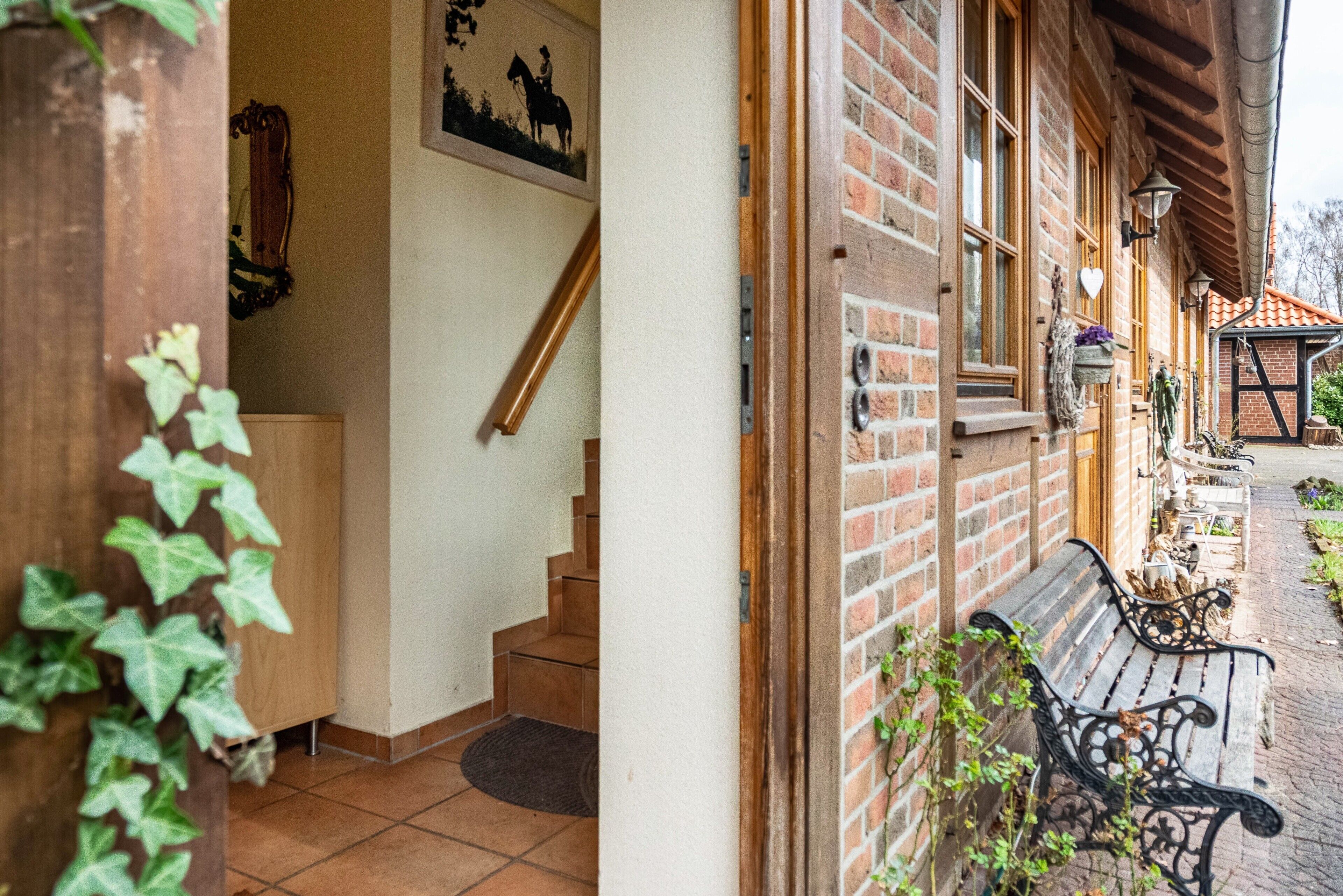 A wooden staircase leading to a room with a door, a bench outside, and a brick wall with a window.