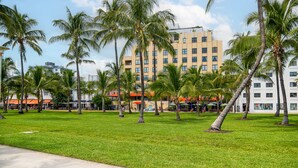 A hotel with a modern building, a grassy area with palm trees, and a clear sky. - The Netherland 2A (Miami Beach)