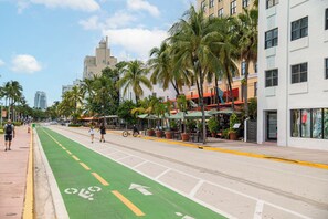 Calle con carril bici, palmeras y edificios con locales comerciales.