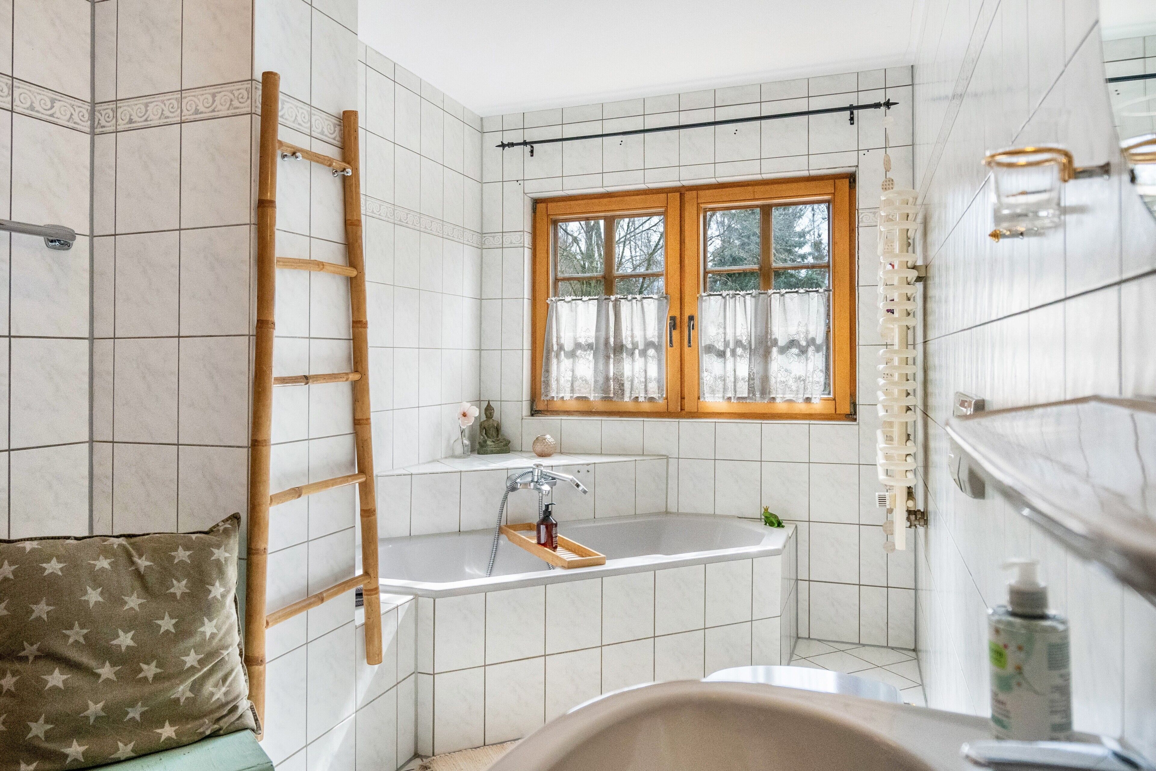 A bathroom with a bathtub, a window with curtains, a towel rack, and a wooden ladder.