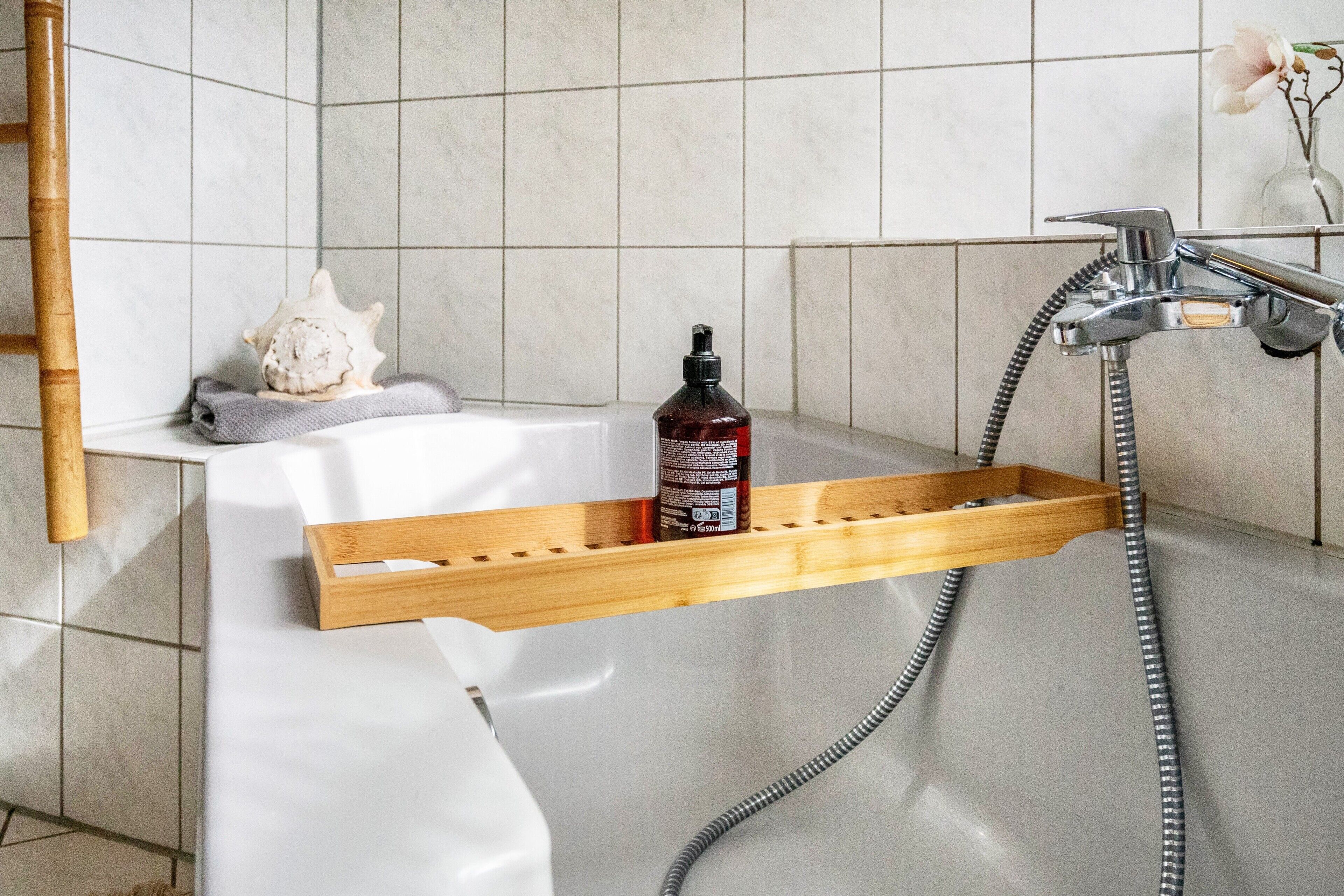Un baño con un estante de madera que contiene una botella, una toalla y una concha marina.