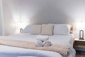 A neatly made bed with white linens, two bedside lamps, and a bedside table.