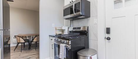 Una cocina moderna con estufa, microondas y horno, una mesa de comedor con sillas y un cubo de basura.