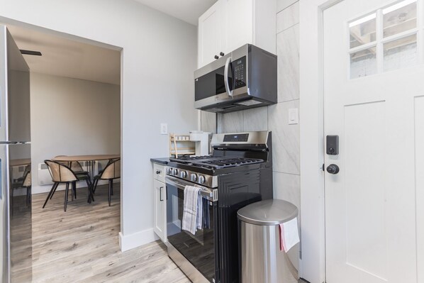 A modern kitchen with a stove, microwave, and oven, a dining table with chairs, and a trash can.