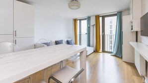 A modern kitchen with a marble countertop, white cabinets, and a dining area with a bench. - Modern King’s Cross Central Apartment (London)
