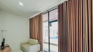 Quarto moderno com sofá, mesa de cabeceira de madeira e uma grande janela com cortinas.