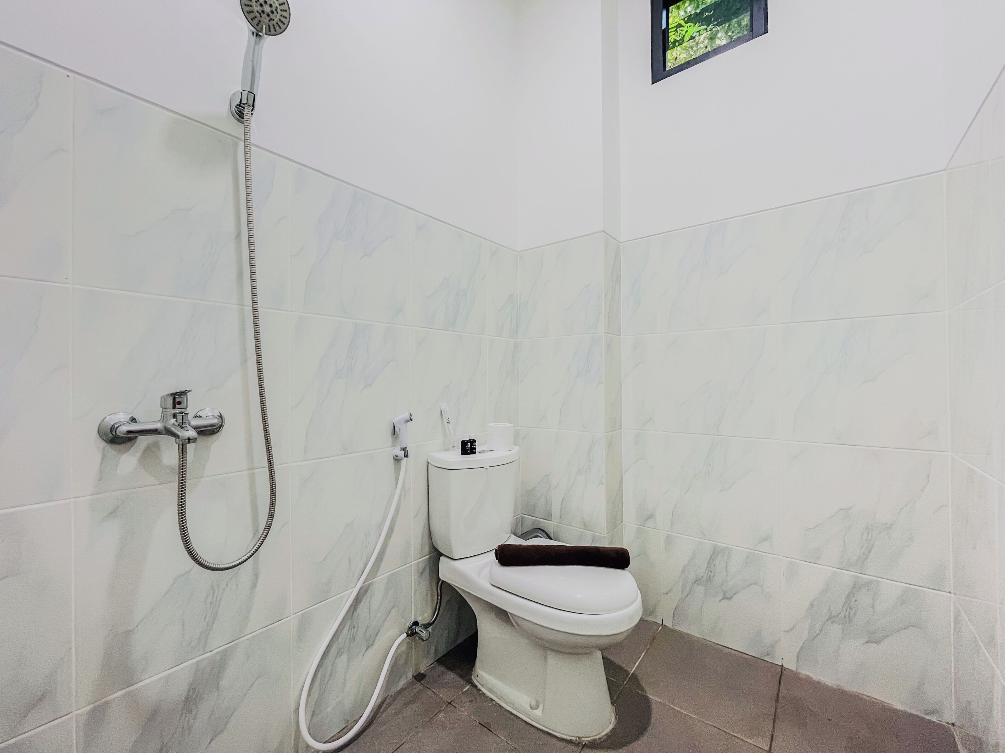 A bathroom with a toilet, a shower, and a small window.