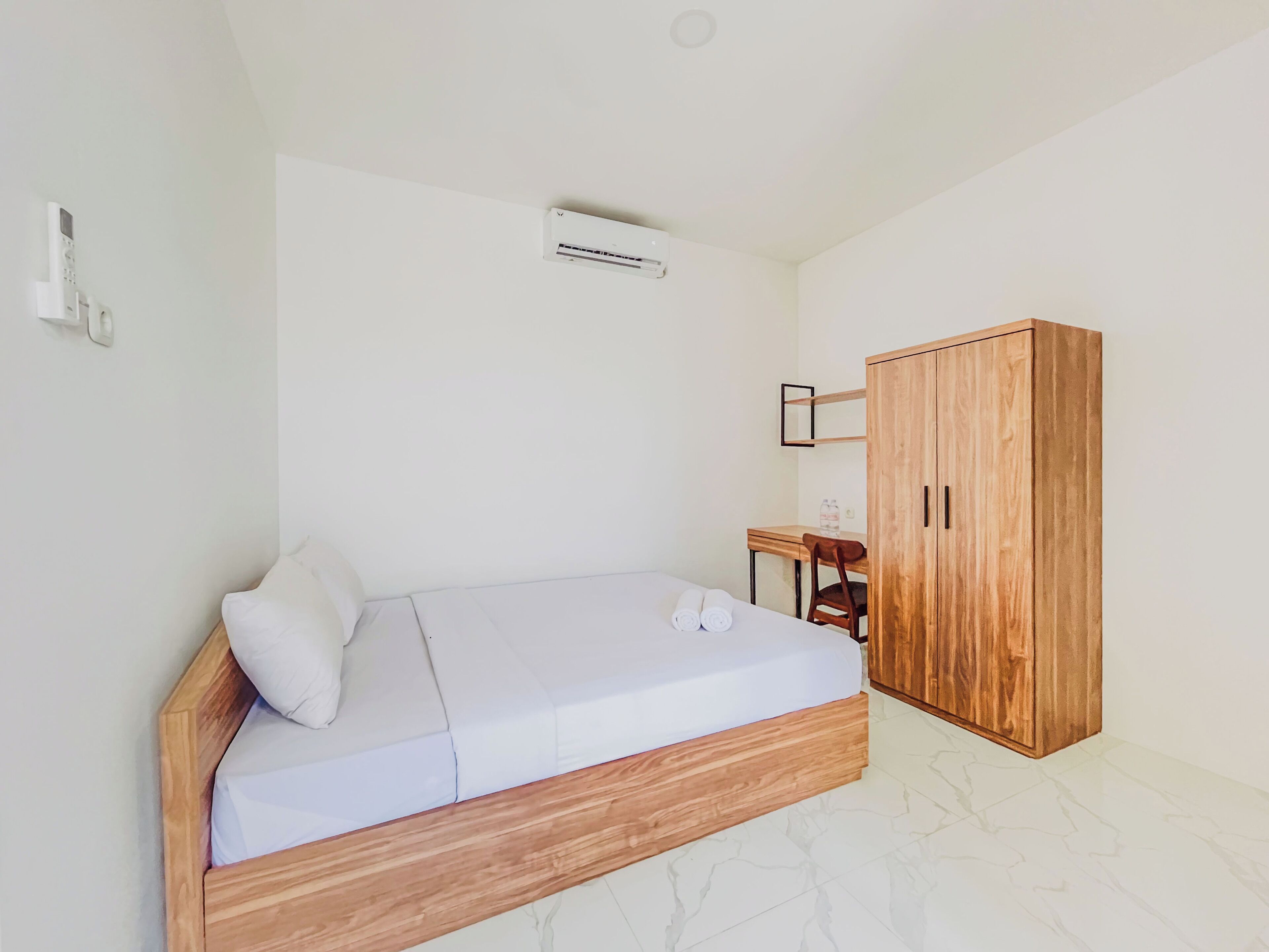 Un dormitorio con una cama de madera, un armario de madera, una mesita con una silla y un equipo de aire acondicionado en la pared.