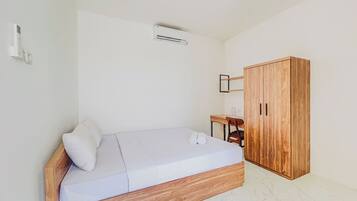 Un dormitorio con una cama de madera, un armario de madera, una mesita con una silla y un equipo de aire acondicionado en la pared.